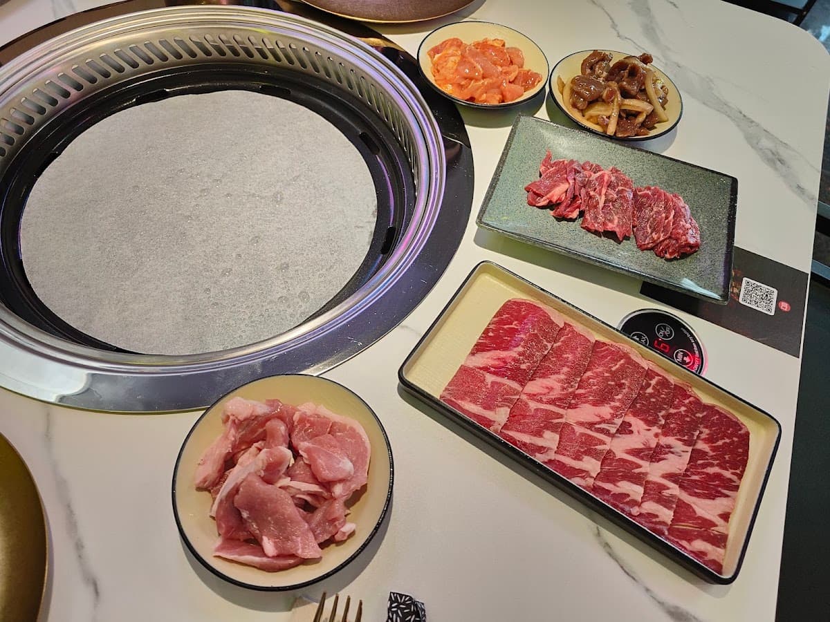 Mesa de Gogi Parrilla con parrilla circular encendida y bandejas de carne coreana marinada lista para asar